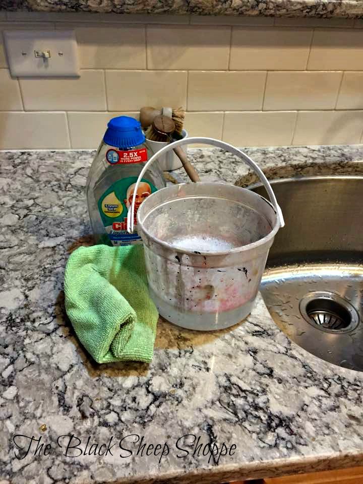 a kitchen counter with a bucket and cleaning supplies on it, next to a sink