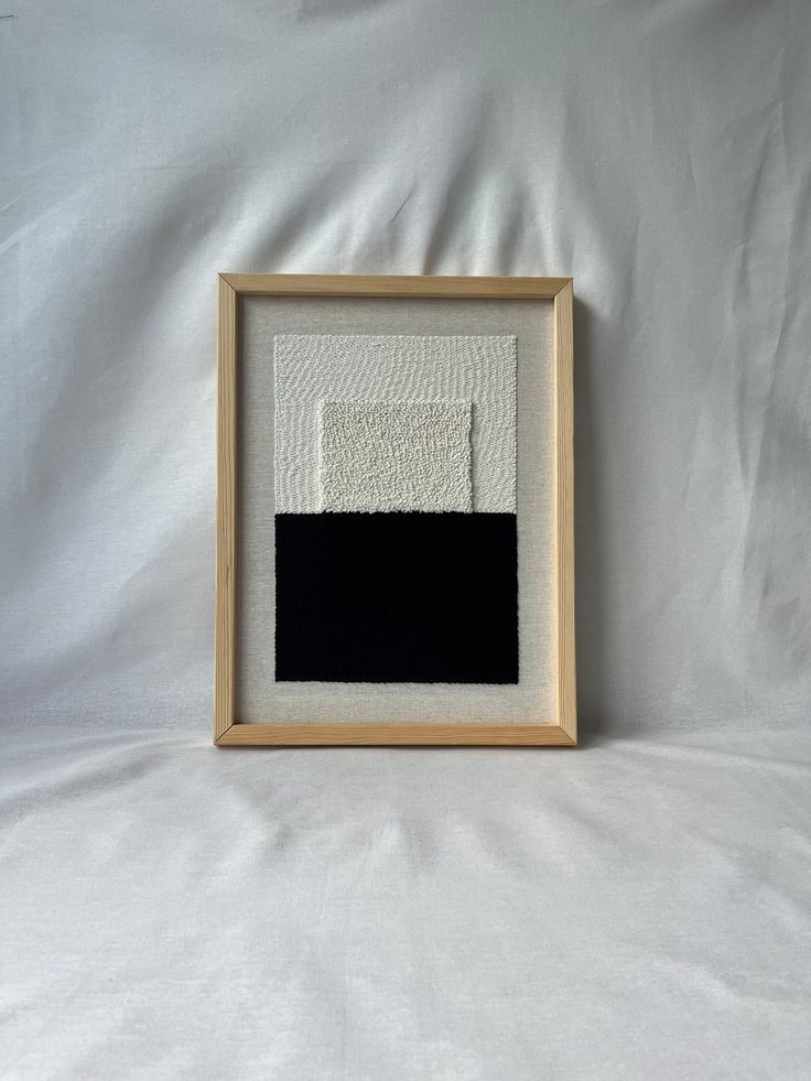 a black and white painting is displayed in a wooden frame on a white sheet background