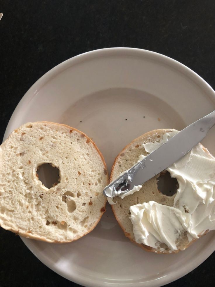 a white plate topped with two bagels covered in frosting next to a knife