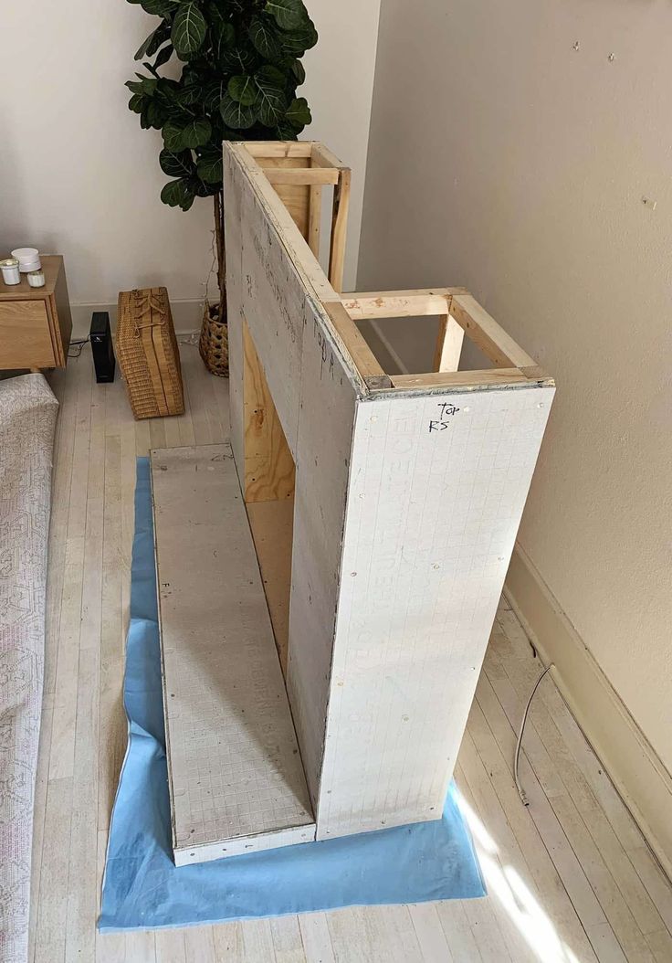 an unfinished wall in the corner of a room with blue tape on it and a potted plant next to it