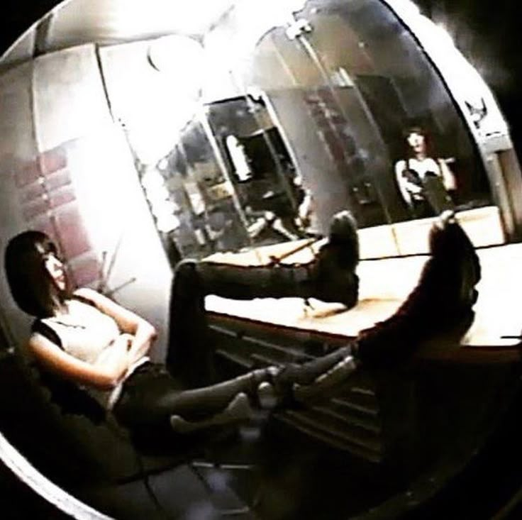 two people sitting in front of a mirror with their feet on the table and one person laying down