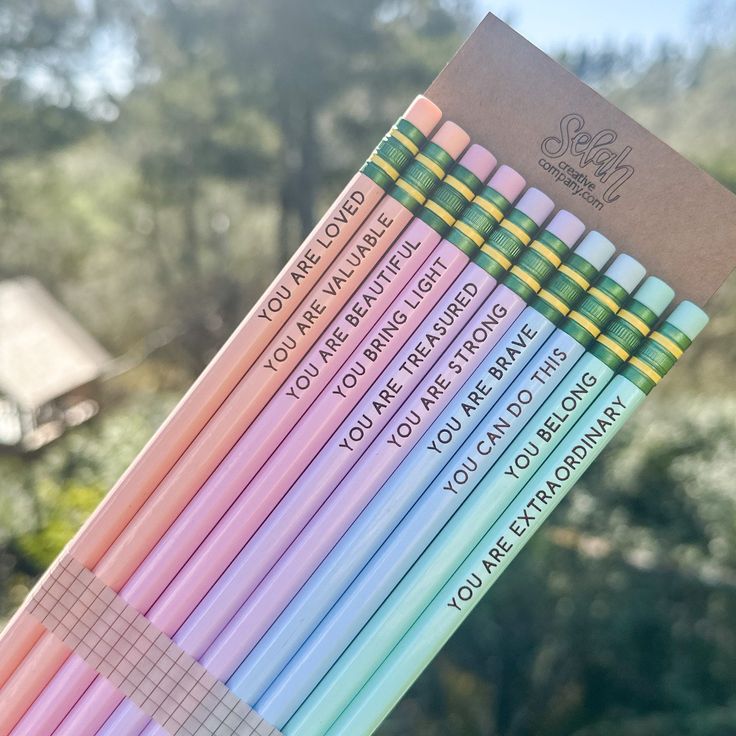 several colored pencils with writing on them in front of some trees and sky background