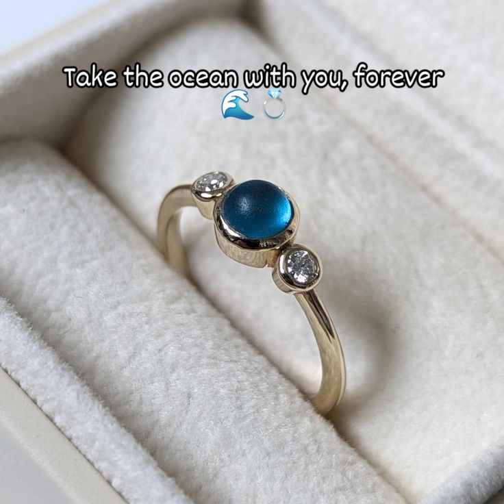 A gold engagement ring featuring a blue sea glass center and two ocean diamonds, displayed in an ivory jewellery box. Holding Something, Engagement And Wedding Ring, Human Hands, Blue Sea Glass, Ring Collection, Human Hand, Gold Engagement Ring, Ring Collections, Gold Engagement