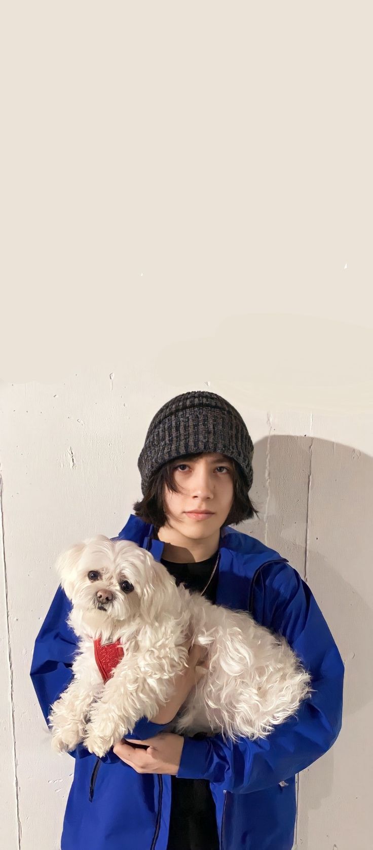 a woman holding a white dog in her arms while wearing a blue coat and hat