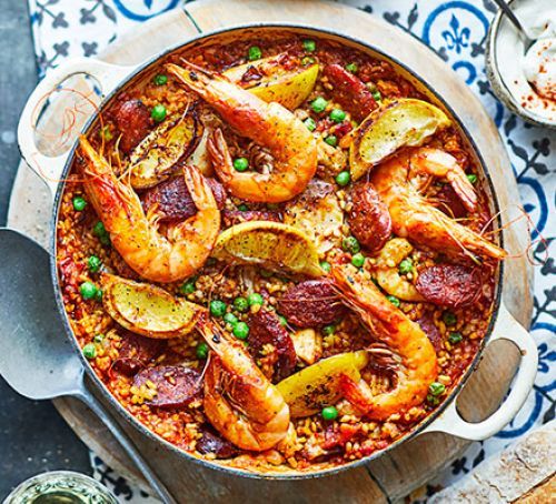 a pan filled with shrimp and peas on top of a wooden table next to bread