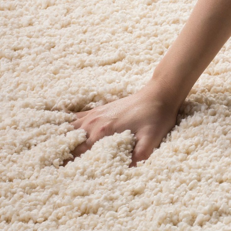 a person's hand is on top of a fluffy white area rug that looks like carpet