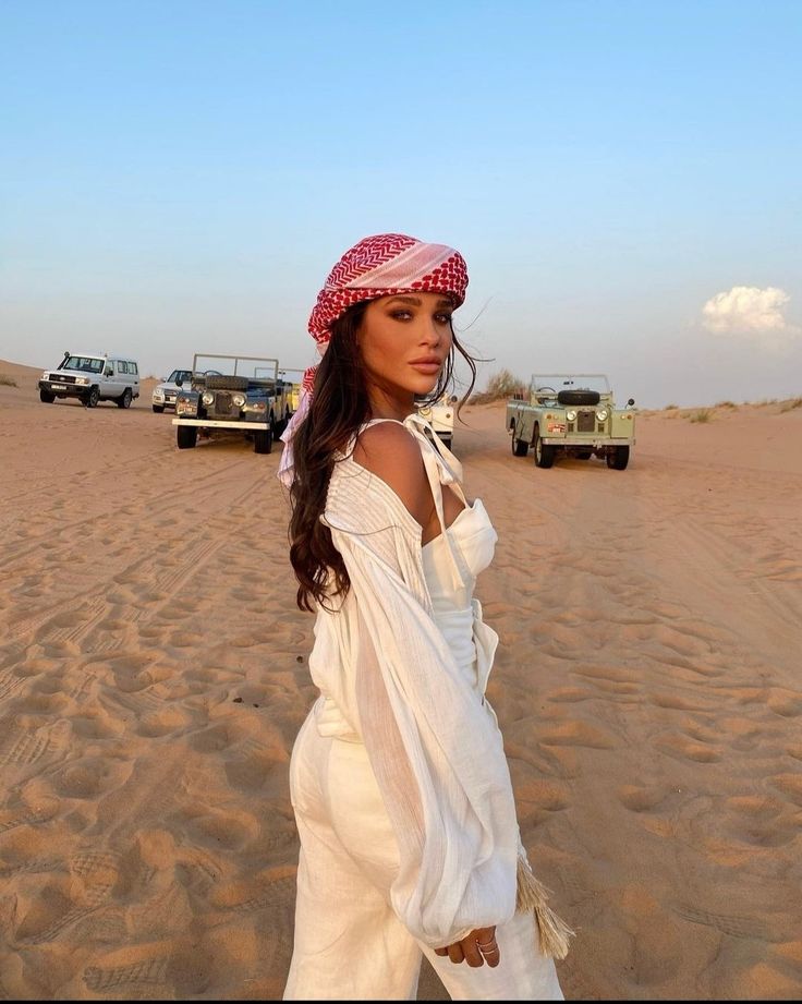 a woman standing on top of a sandy beach next to a green truck and jeep