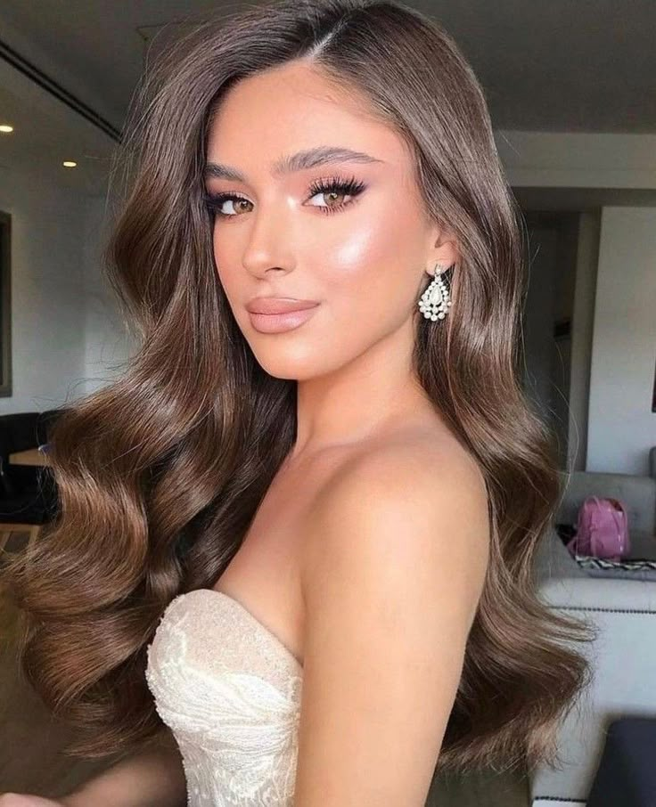 a woman with long brown hair wearing a strapless dress and earrings, posing for the camera