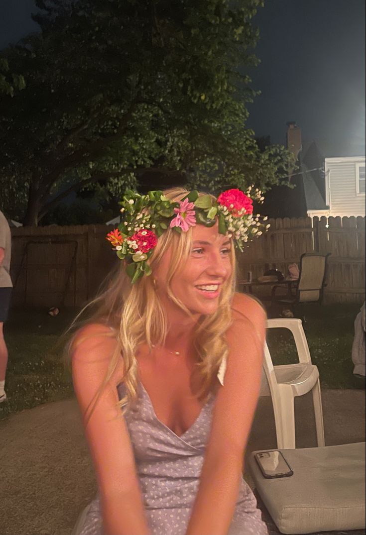 a woman with flowers in her hair sitting on a chair outside at night smiling for the camera