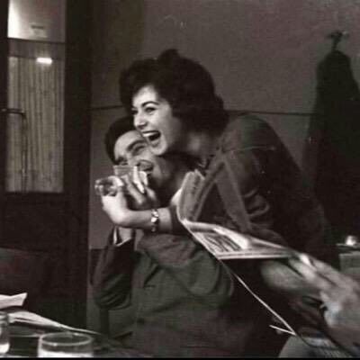 two women laughing while sitting at a table with papers and drinks in front of them