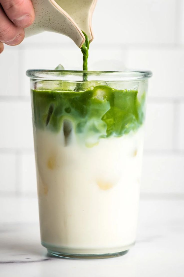 someone pouring green liquid into a glass with lettuce in it on a white counter