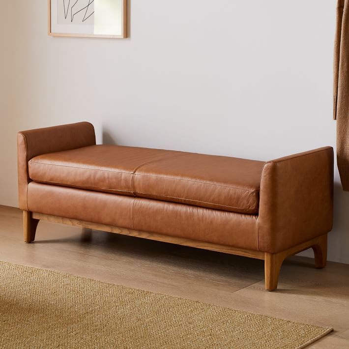 a brown leather couch sitting on top of a hard wood floor next to a window