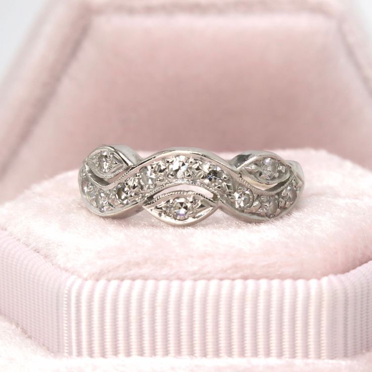 a white gold ring with diamonds in it sitting on a pink velvet cushioned box