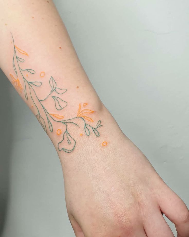 a woman's hand with an orange and green tattoo on her left wrist,