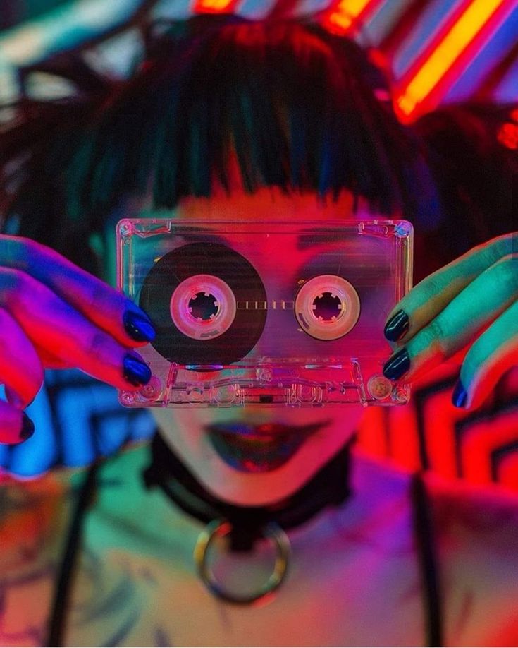 a woman holding up a cassette in front of her face with two eyeballs on it