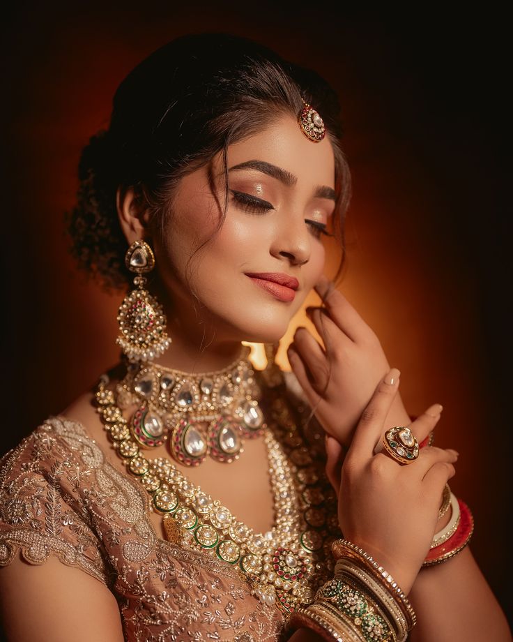 a woman in a bridal outfit with jewelry on her neck and hands near her face