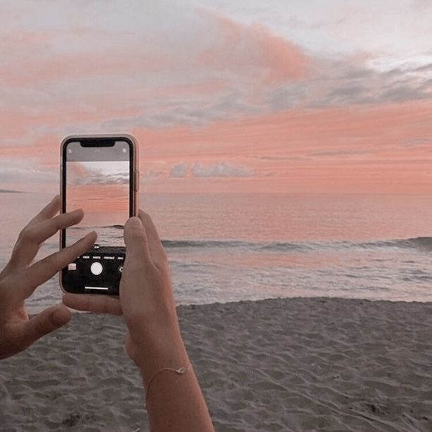 a person taking a photo with their cell phone on the beach at sunset or sunrise