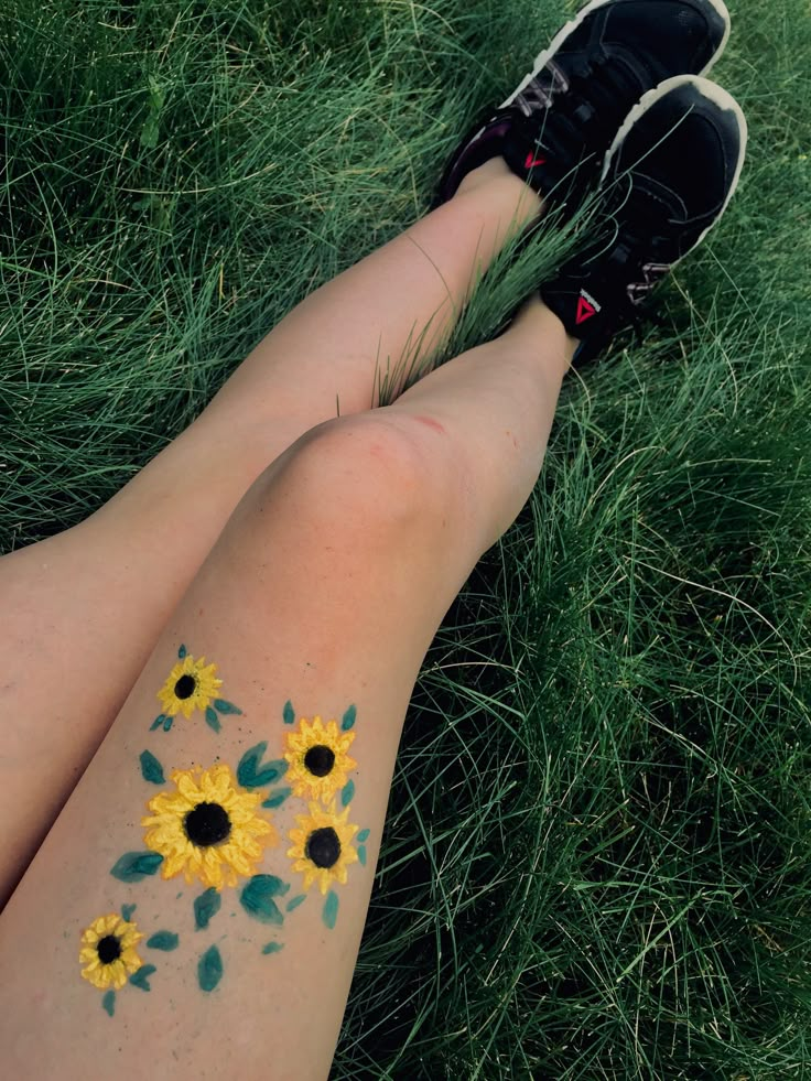 a person laying in the grass with sunflowers painted on their legs and feet