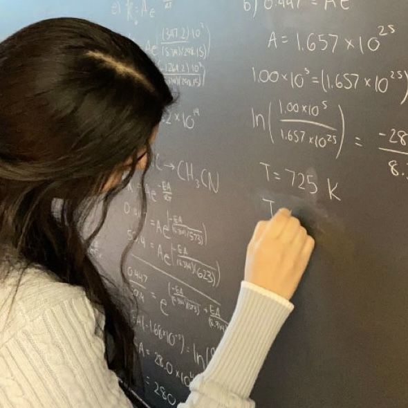 a woman writing on a blackboard with numbers and formulas written on the board