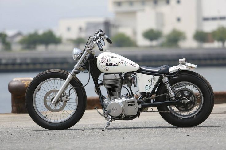 a white and black motorcycle parked next to a body of water with buildings in the background