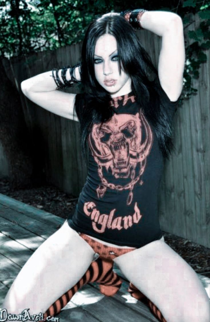 a woman with long black hair sitting on a wooden bench wearing an orange and black shirt