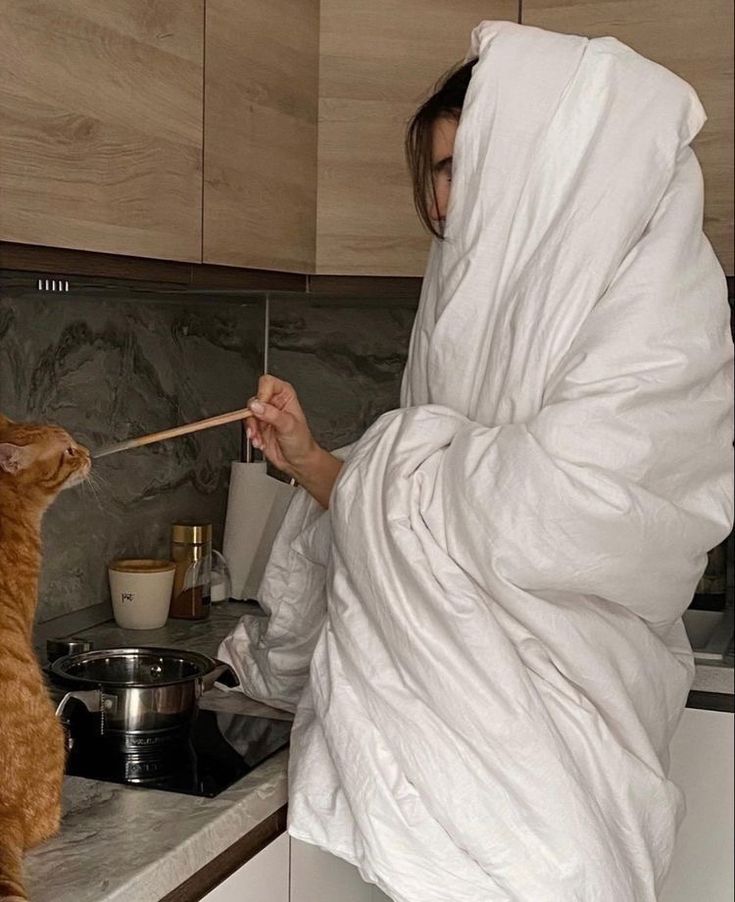 a woman in a bathrobe is feeding a cat