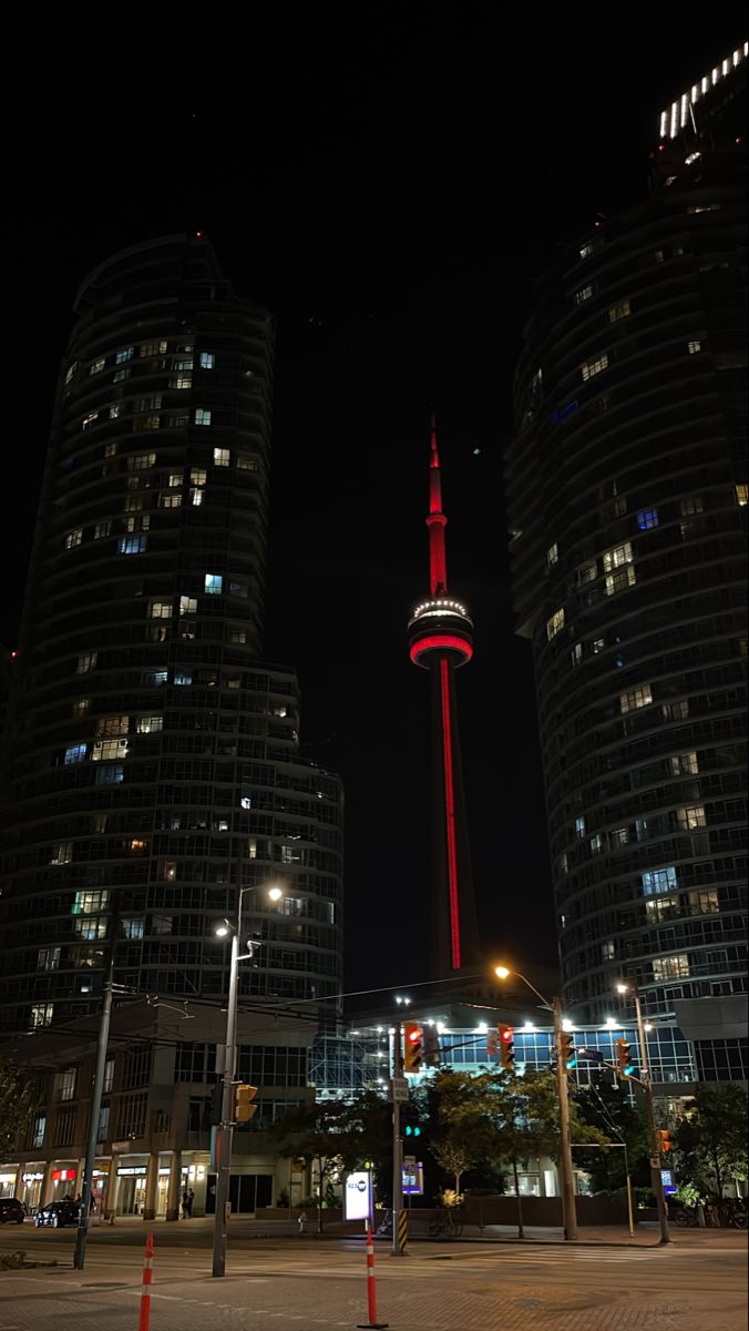 tall buildings are lit up at night in the background, and there is a red light on top