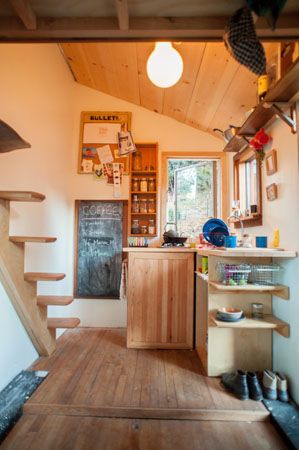 the inside of a tiny house with wood floors and stairs leading up to an open kitchen area