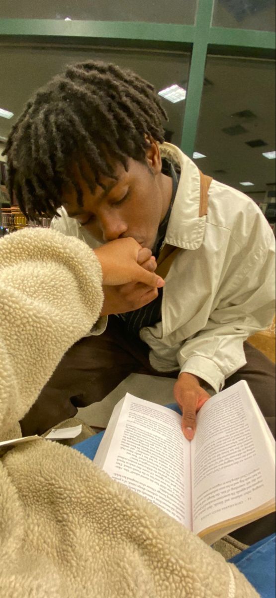 a man reading a book while sitting on the floor next to another person with his hand over his mouth