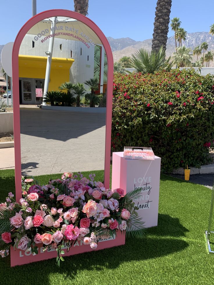 a pink mirror sitting on top of a lush green field next to a flower pot