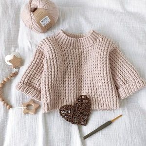 a knitted sweater and crochet accessories are laid out on a bed next to a ball of yarn