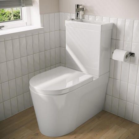 a white toilet sitting next to a window in a bathroom with wooden floors and tile walls