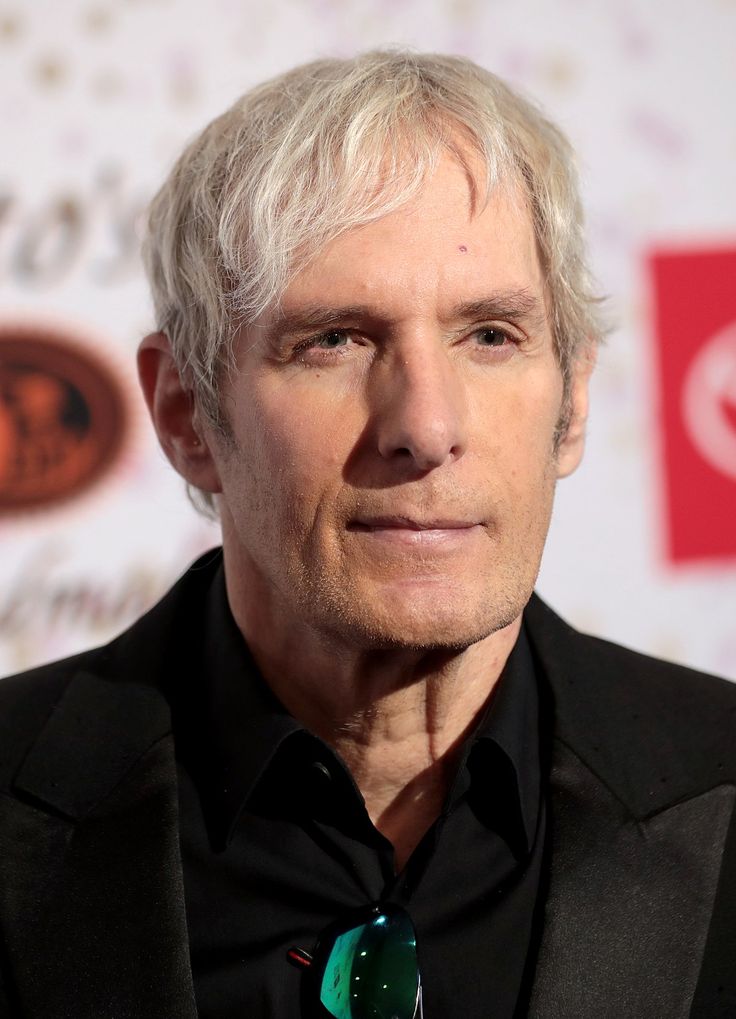 an older man with white hair wearing a black suit and green tie, looking at the camera