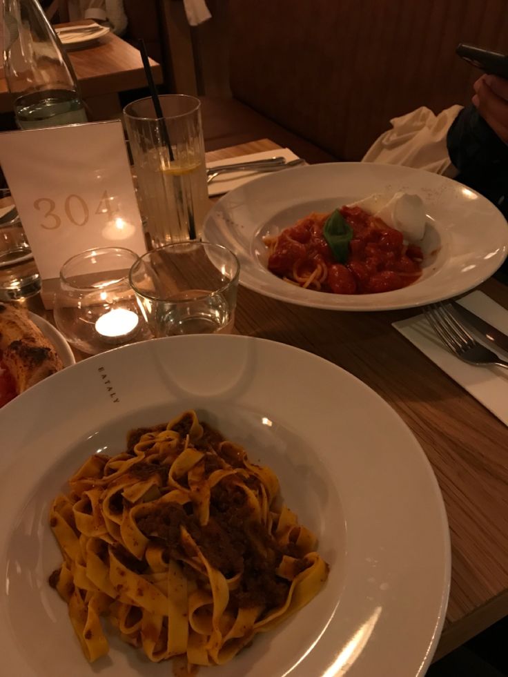 a plate of pasta with meat and sauce next to a glass of water on a table