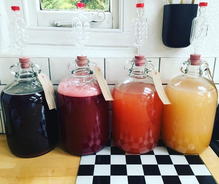 four different colored drinks in glass jugs sitting on a checkerboard counter top