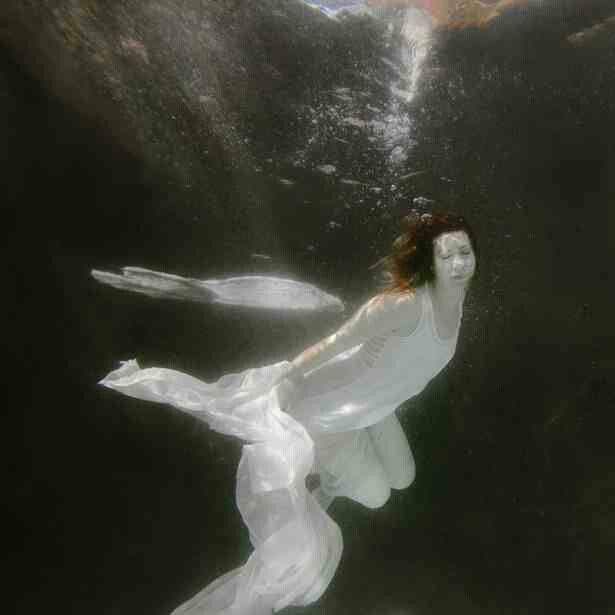 a woman is floating in the water wearing a white dress