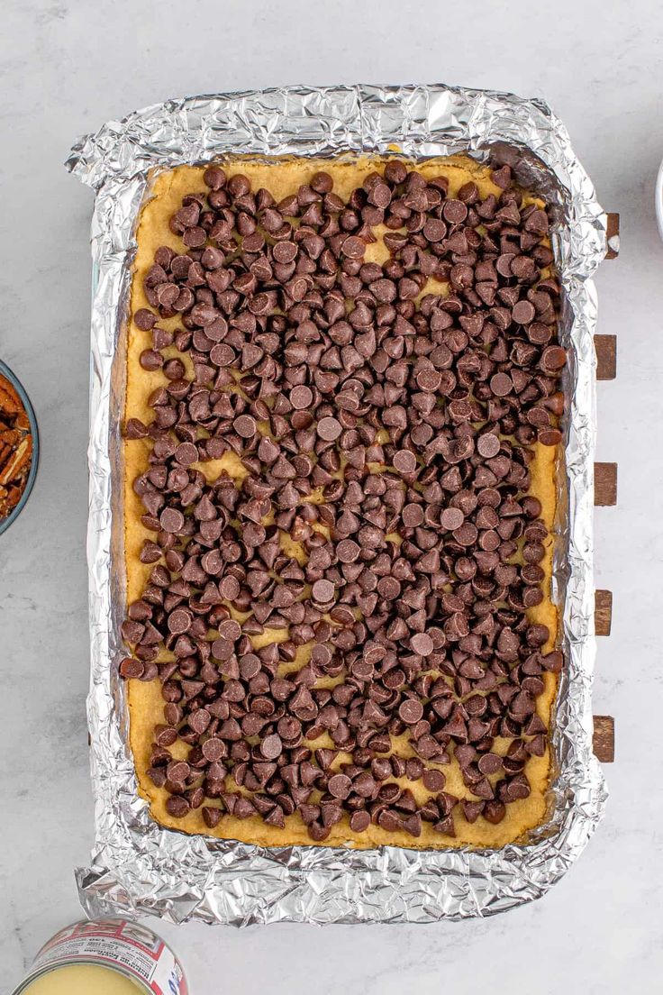 chocolate chips on top of an uncooked cookie crust in a baking pan next to other ingredients