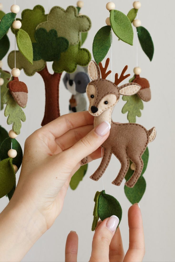 a hand holding a small stuffed animal in front of a mobile with trees and animals on it