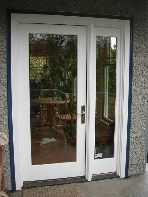 a dog laying on the ground in front of a white double door with glass panels