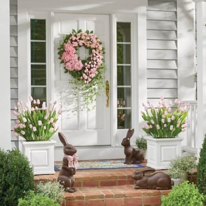 two bunny statues sitting in front of a white door with pink flowers and wreath on it