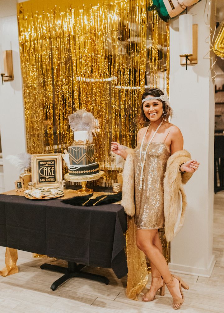 a woman standing in front of a table with a cake and gold decorations on it