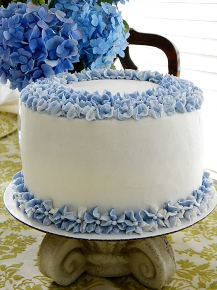 a white and blue cake sitting on top of a table next to a vase filled with flowers