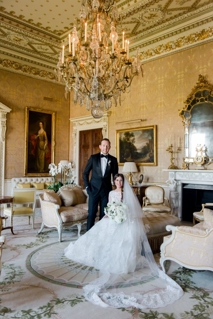 a bride and groom pose for a photo in the formal sitting room with chandelier