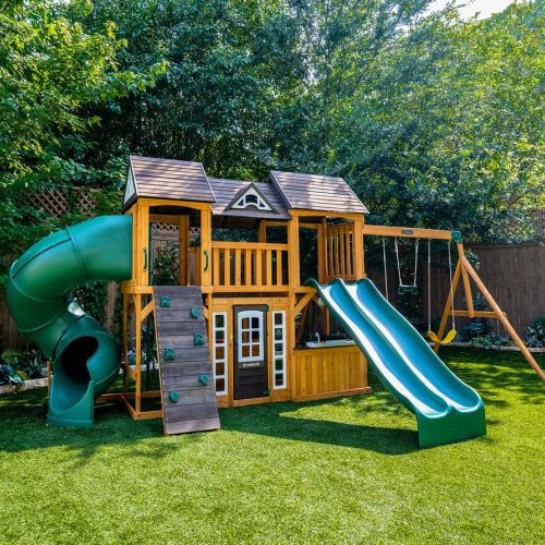 a wooden playset with a slide and green slides in the grass next to trees