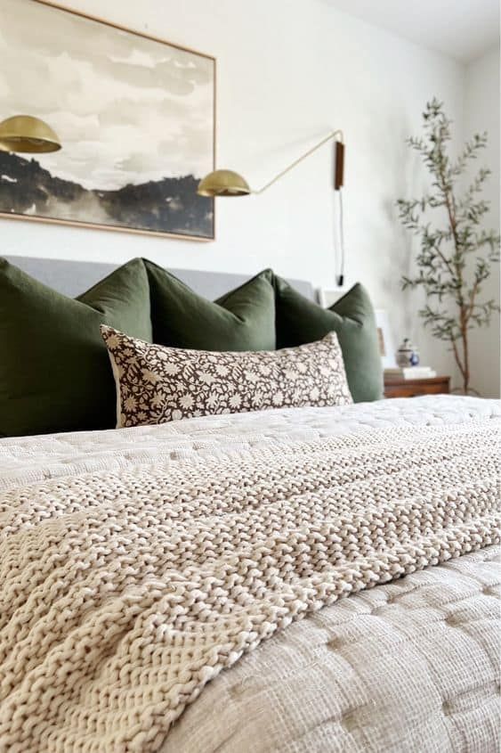 a bed with green pillows and blankets in a bedroom next to a painting on the wall