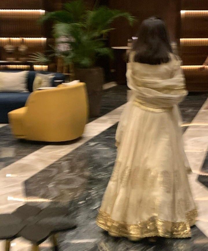 a woman in a white and gold dress walking through a lobby