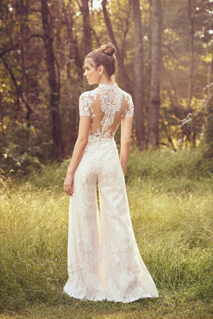 a woman standing in the grass with her back to the camera, wearing a wedding dress