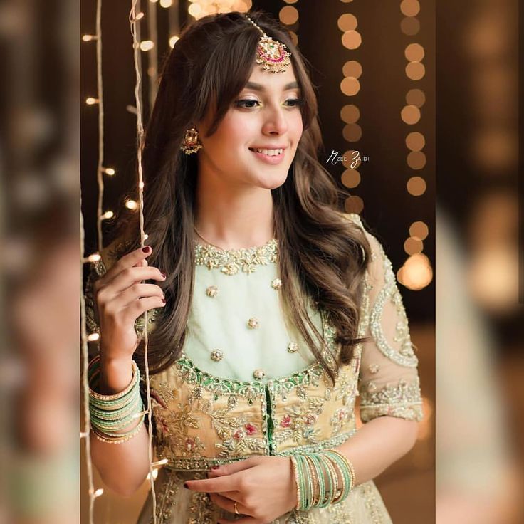 a woman in a green and gold outfit smiling at the camera with lights behind her