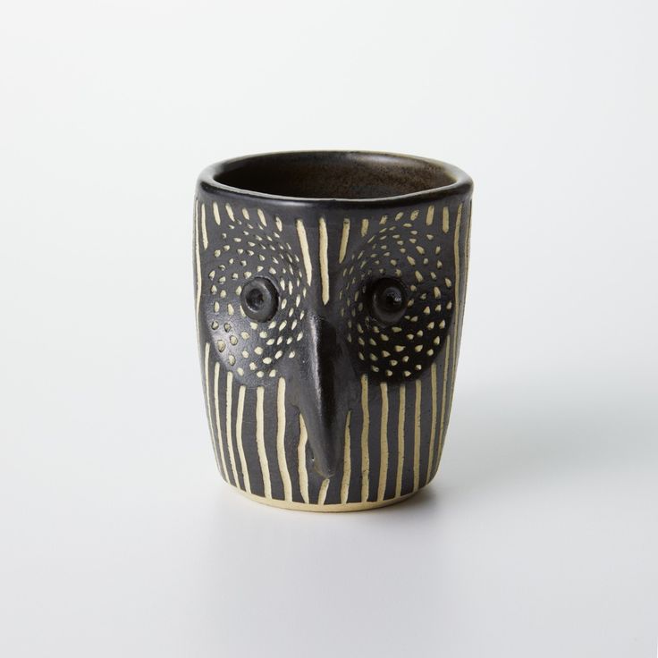 a black and white cup with an owl's face painted on the side, in front of a white background