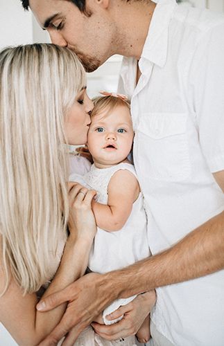 a man and woman holding a baby in their arms while they are kissing each other